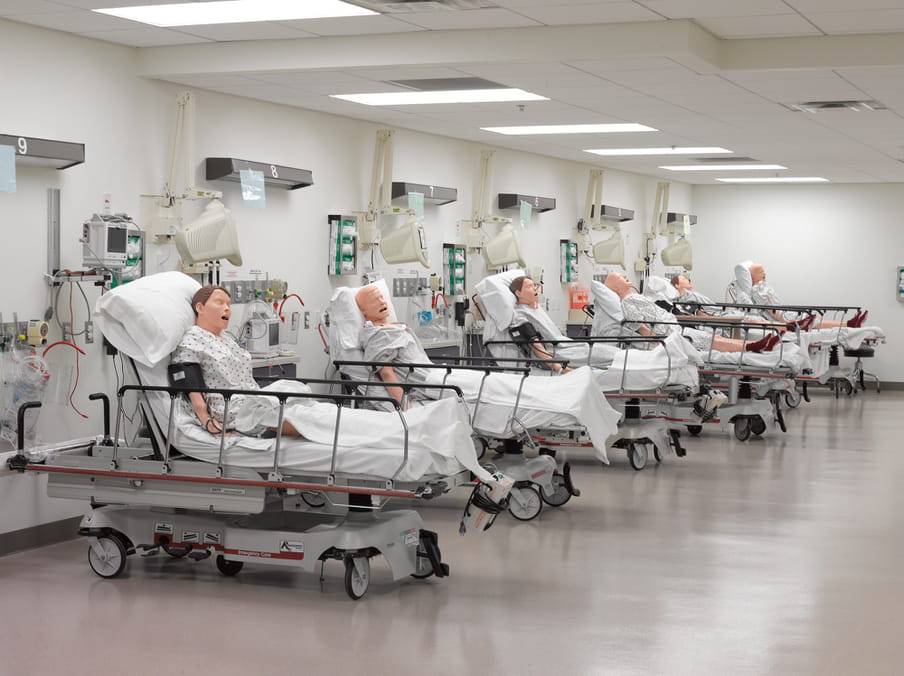 Photo of row with six hospital beds, all occupied by male dolls.