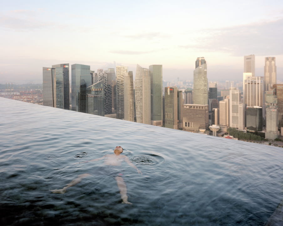 Picture of a man floating in a large pool overlooking a city skyline