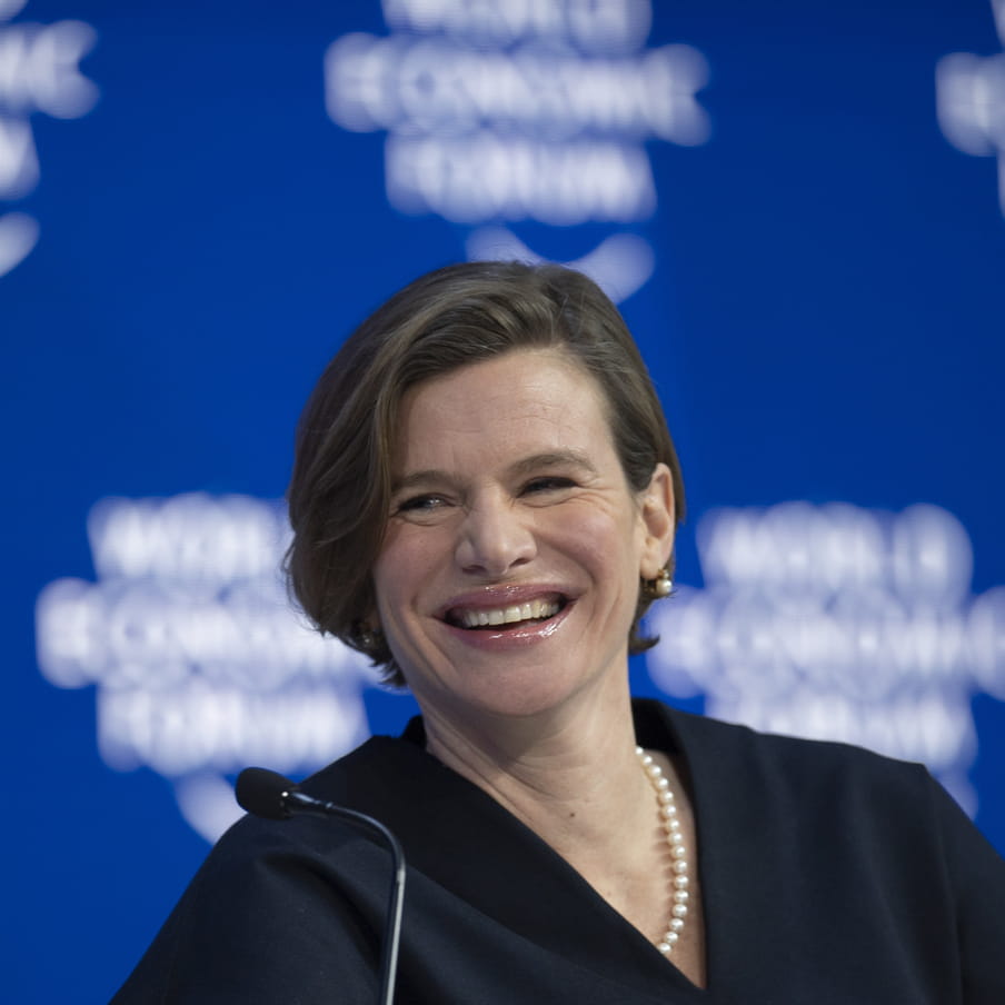 Photo of a woman smiling in front of a blue screen stating ‘world economic forum’