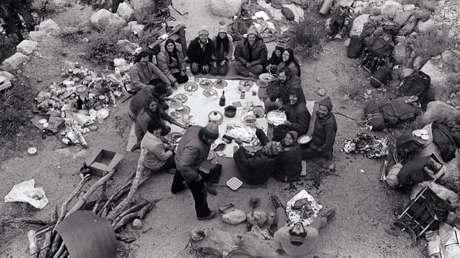Black and white photo of a group of people sit on the floor in nature, having a picnic