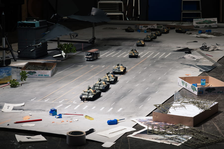 Diaromas of a row of army tanks, in a photo studio, with props laying around.
