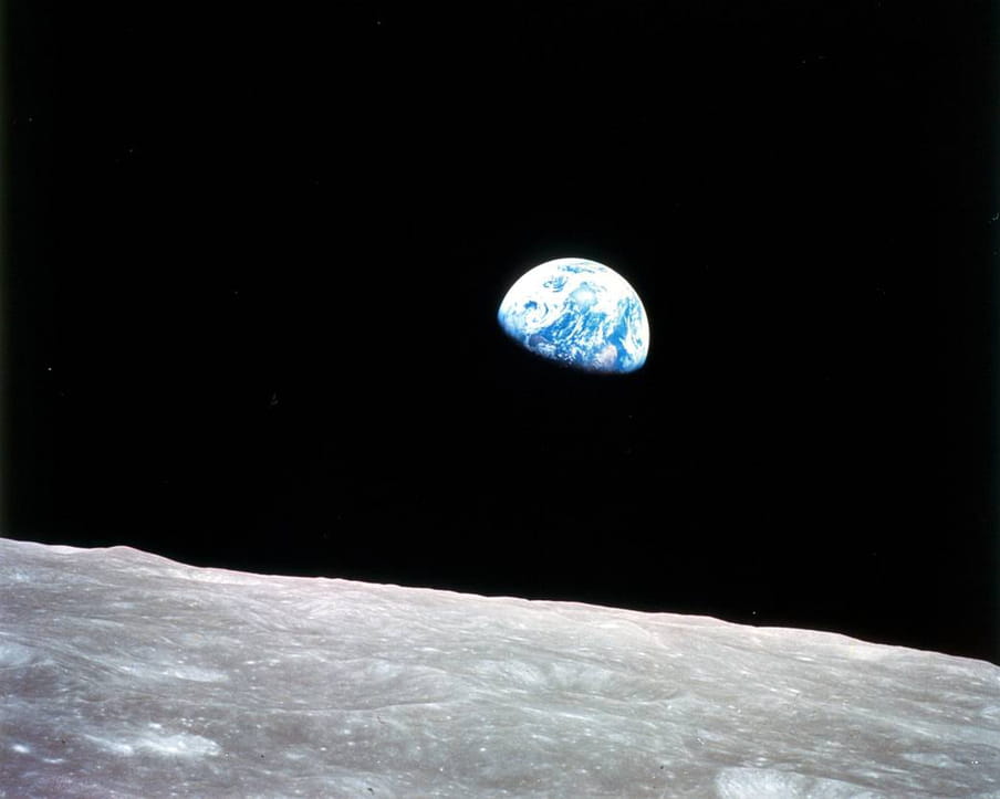 Photo taken from outer space of the blue and white planet Earth, seen hovering above a desolate lunar surface in the foreground.