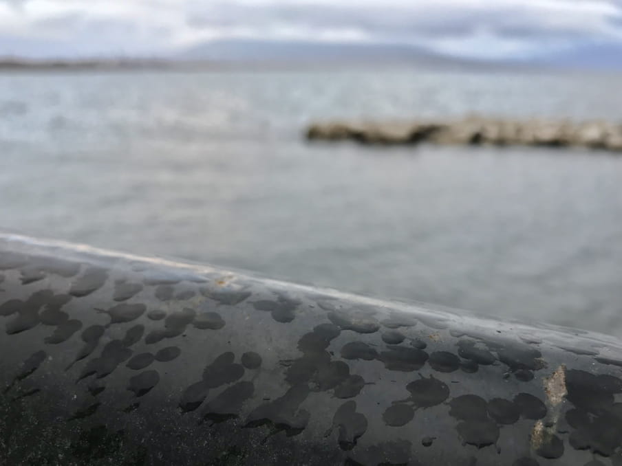 In the image there is a railing in the foreground with raindrops on it, and in the background the sea, with Mt Vesuvius sketched and hidden by clouds on the horizon.