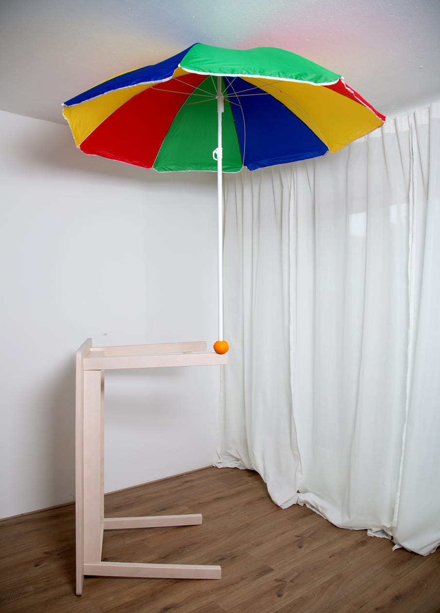 Picture of a wooden table holding up a structure compsed by an orange and a beach umbrella