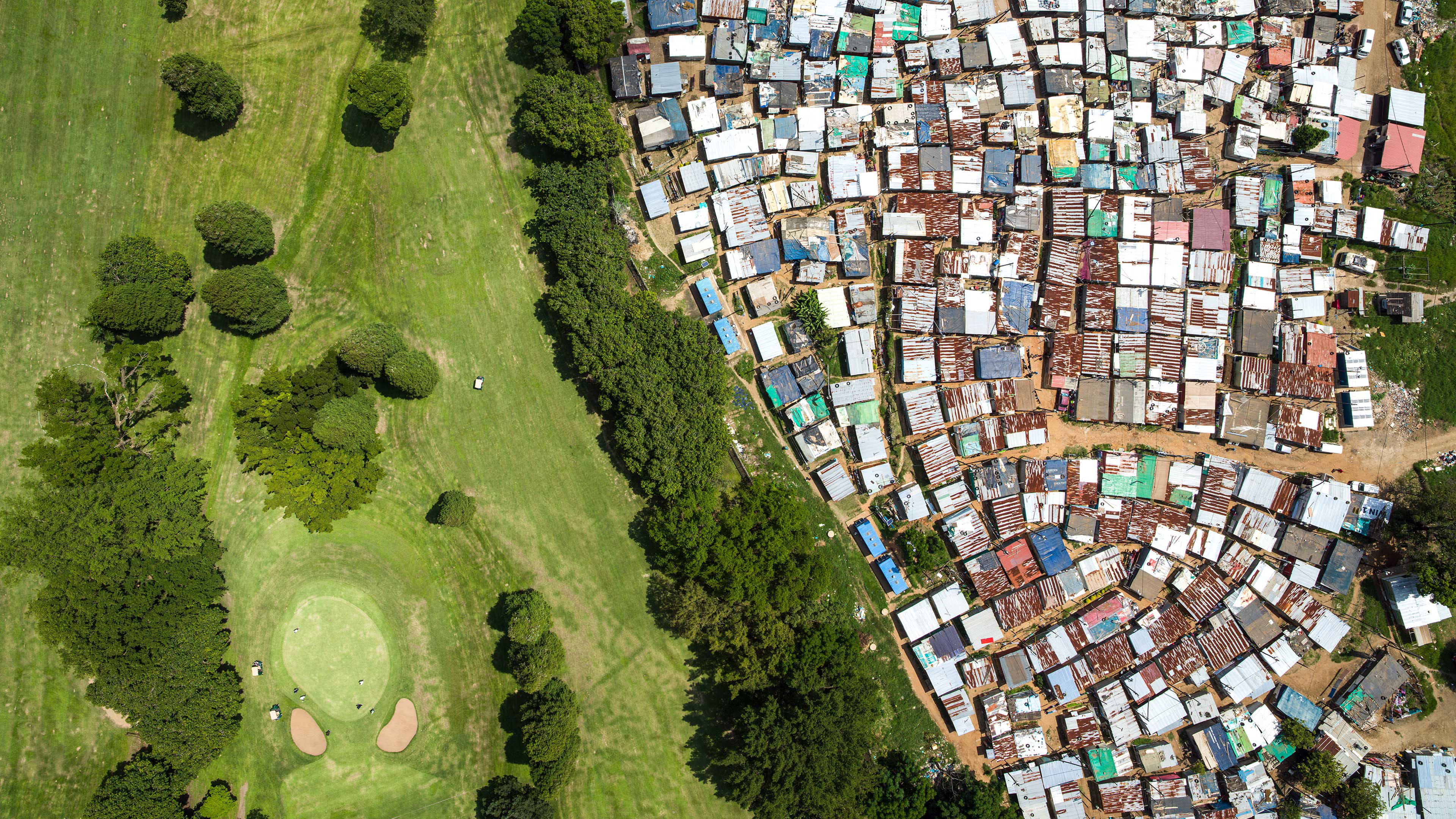 Drone photo of a land. On the right a shanty town, on the left a residential aerea.