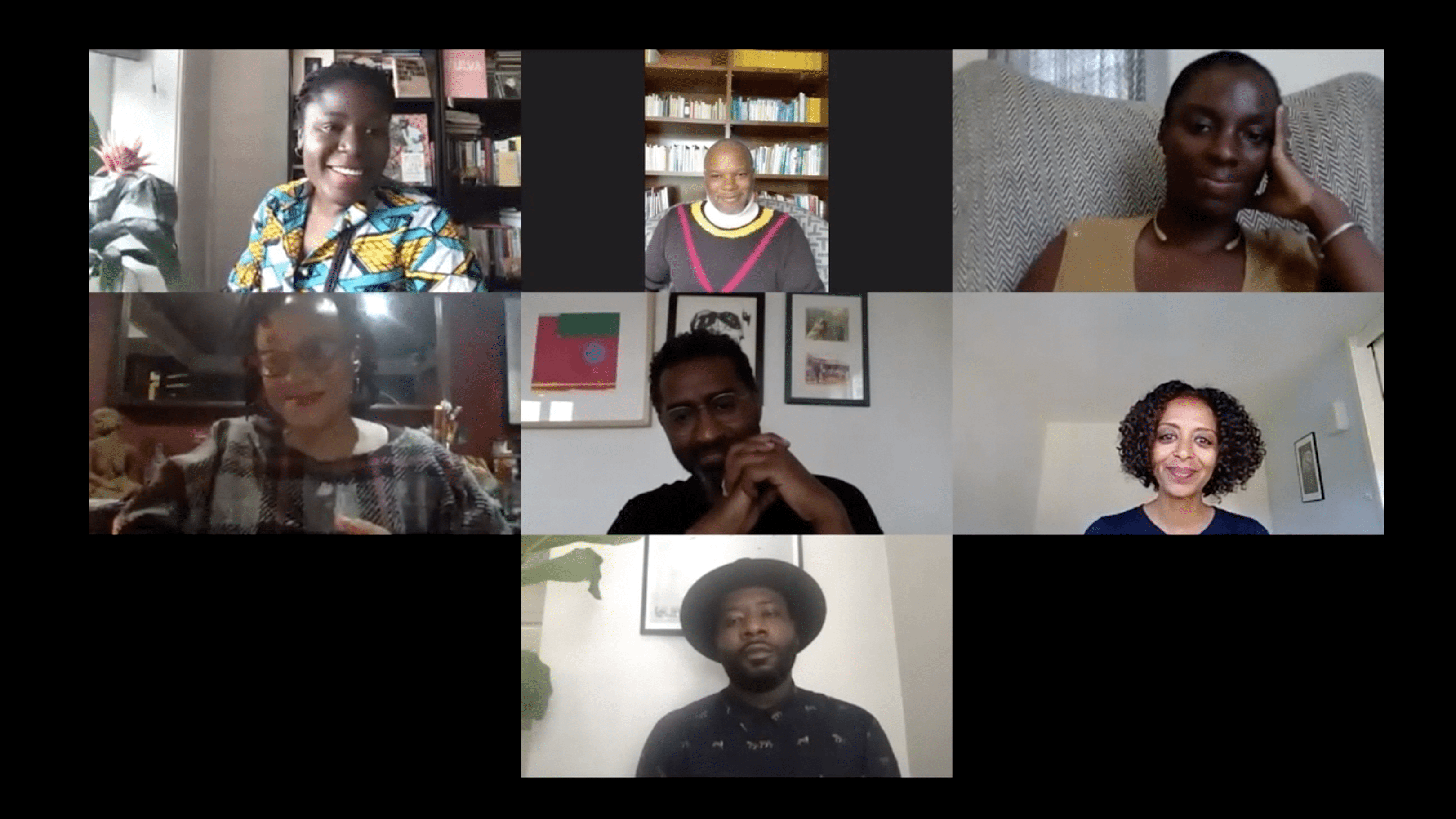 Seven head shots of persons in rectangular video screens lined up one against the other, in a three: three: one format. From top left to bottom: face smiles in colourful green and yellow shirt; person with a red V on their jumper against a bookshelf; smiling person leaning head on hand; slightly blurry smiling person; person with hands clasped against photo frames; person smiles at camer; and below, a person in a hat against a photo frame