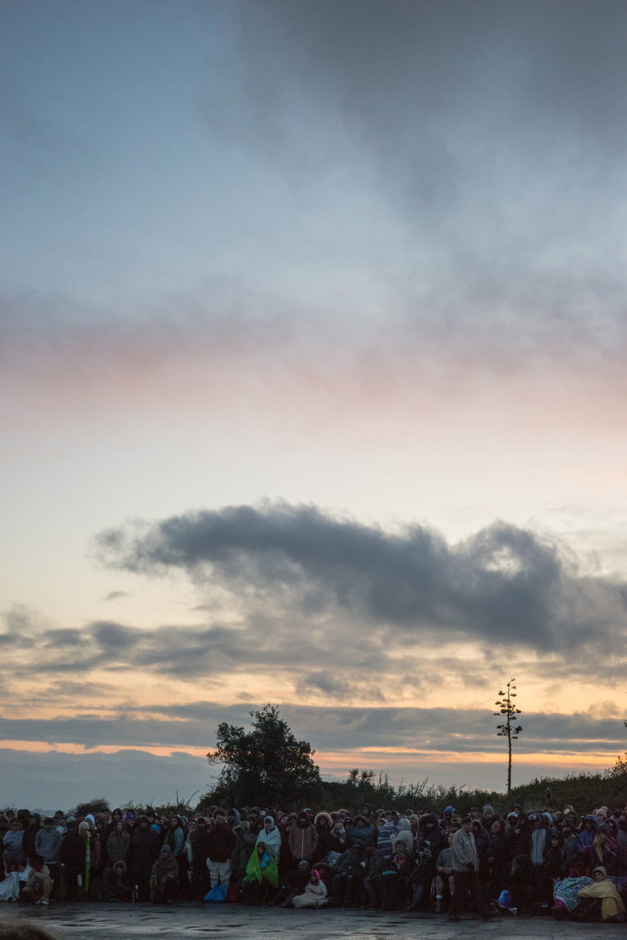 Group of people wearing sheets and rain coats in front of a orange sky as the sun goes down