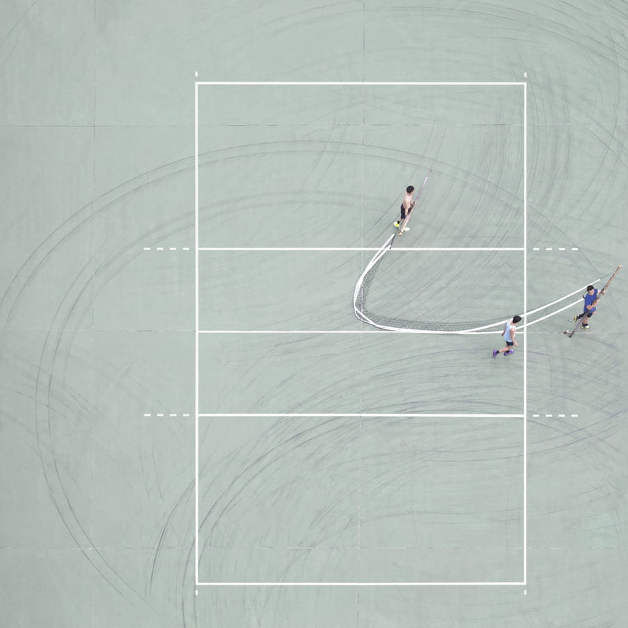 Photograph taken from above of three men transporting a net on a mint green ground court.