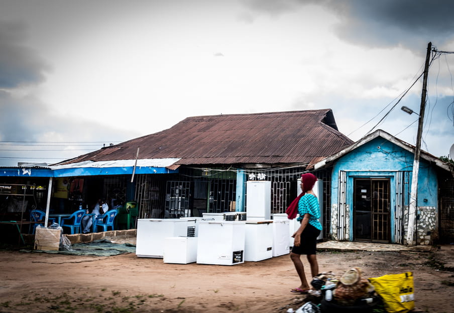 Photo of a shop with fridges standing in front of it, and a woman walking by