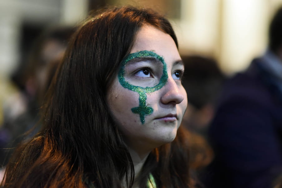 Photo of a girl looking up, a green venus symbol painted in green glitter around her eye