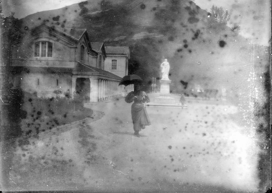 Old damaged photograph of a woman standing with an umbrella