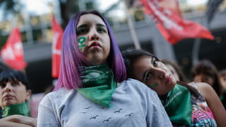 Photo of two girls at a demonstration, one with dark hair and one with purple hair, both wearing green bandanas around their neck
