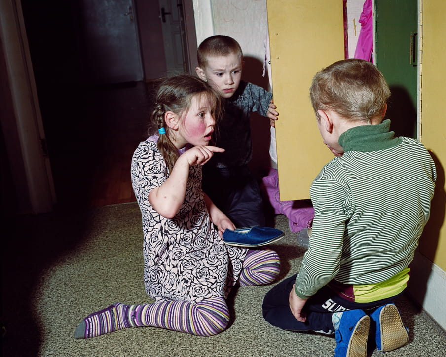 Photo of three kids playing, one girl holding one shoe is pointing her forefinger toward one of the two boys.
