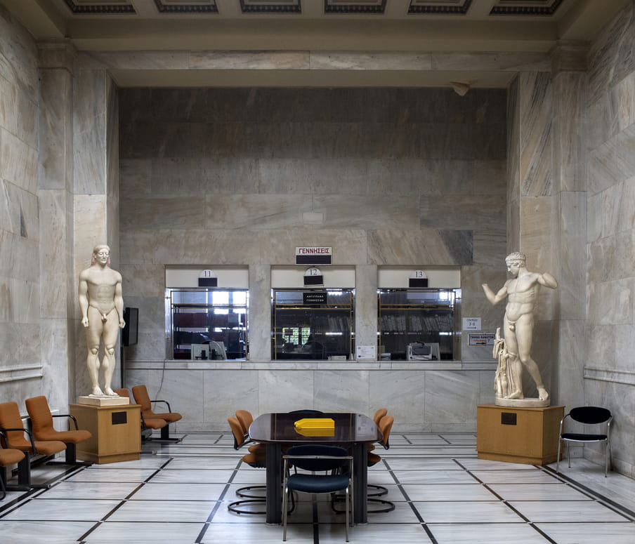 Two classical Greek statues in the corners of a large lobby of an office building in Athens. 