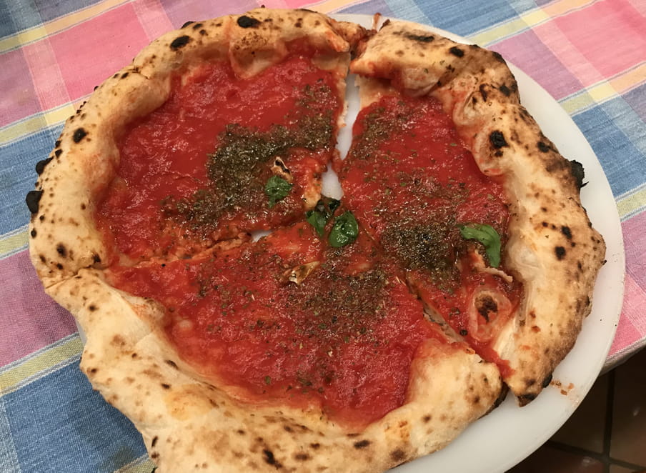 There is a marinara pizza, with tomato sauce, garlic and oregano, on a white dish, on a checkered tablecloth.
