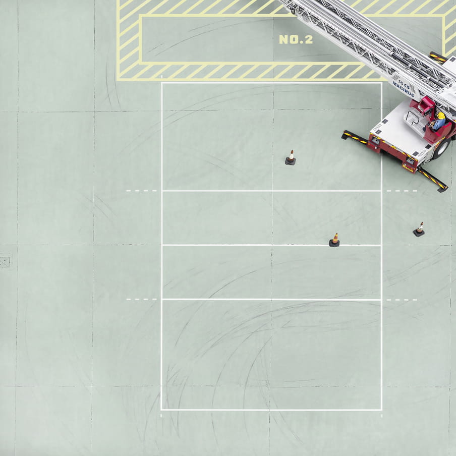 Photograph taken from above on a mint green court showing a firemen in a truck.