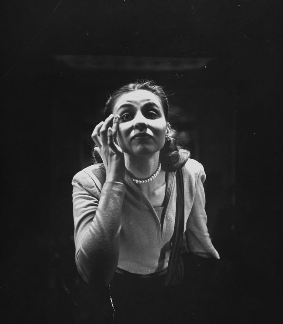 Old black and white photo of a woman checking her make up in a mirror, shot from the back of the mirror