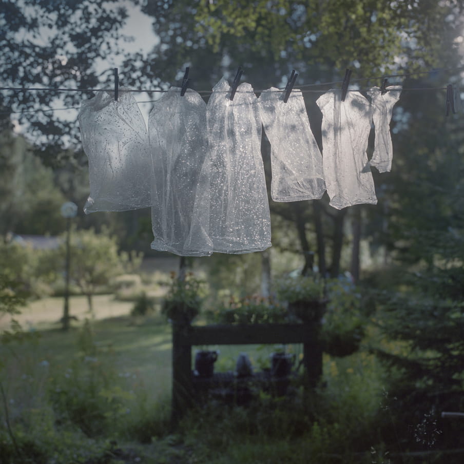 Photograph of plastic bags that are hanging on a line to dry in a green surrounding. 