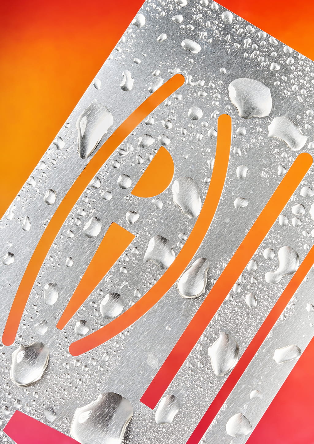 Photograph of a metallic stencil covered with drops of water on a pink and orange gradient background. 