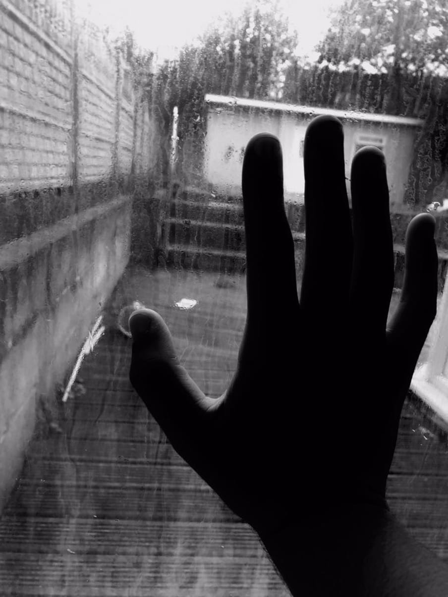 A hand is photographed against a window, with a back garden in the background.