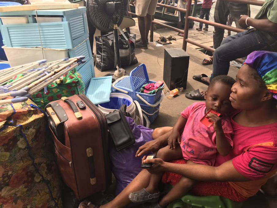 A woman and small child sit on the ground next to suitcases and other belongings.