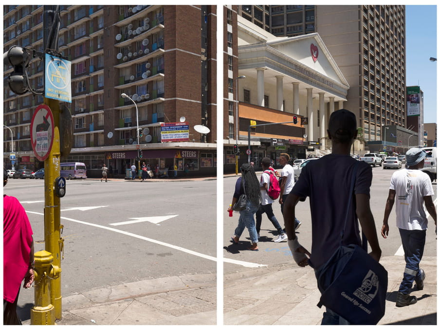 A picture of people crossing a road - in the background a tall buildings and a sign of a local store that reads "STEERS"