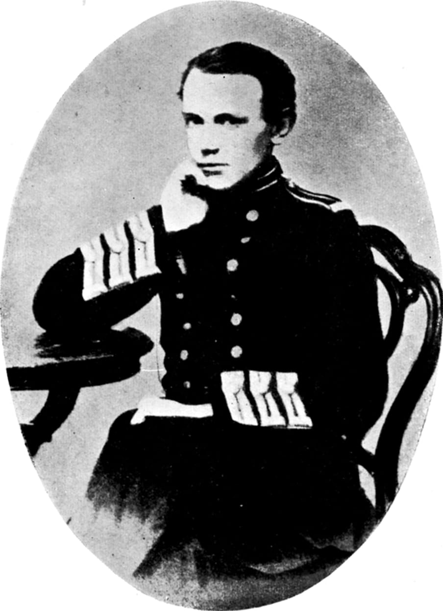 Black and white archival photograph of a young man in uniform, sitting with his elbow on a table and his hand under his chin. 