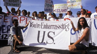 Old photo of people protesting with signs, the biggest one stating 'You're Embarrassing U.S.'