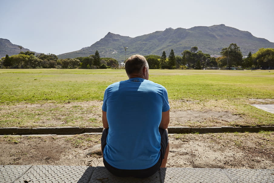 Photo of a man sitting down, looking at a field with mountains in the back