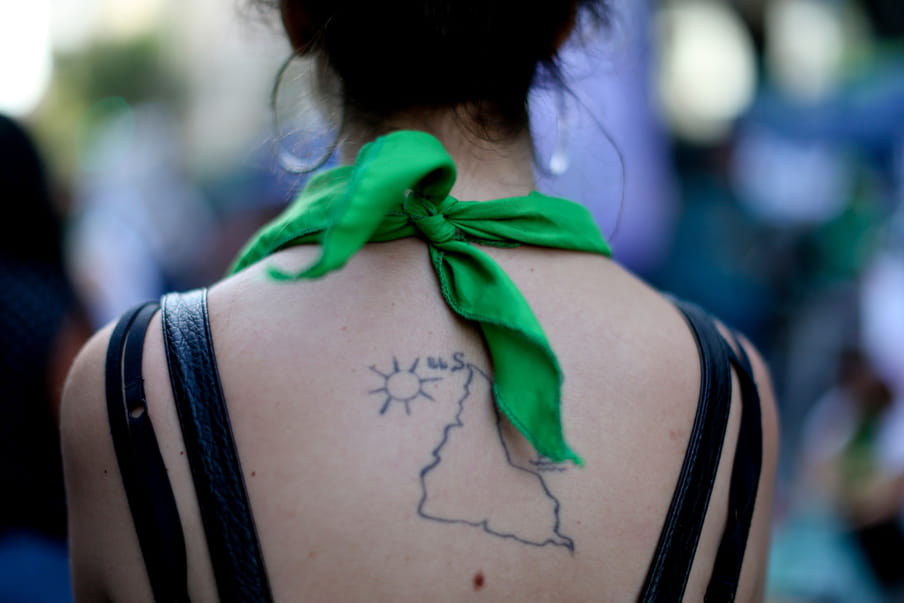 Photo of a the back of a woman with a tattoo of South America, she’s wearing a green bandana 