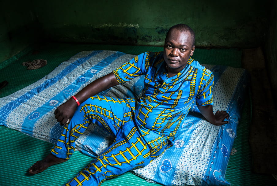 Photo of a man in a blue and yellow outfit sitting on a mattress on the floor