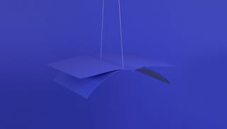 Photo of a few blue pages weaved together into a book, hanging from a string in the air - on a blue background