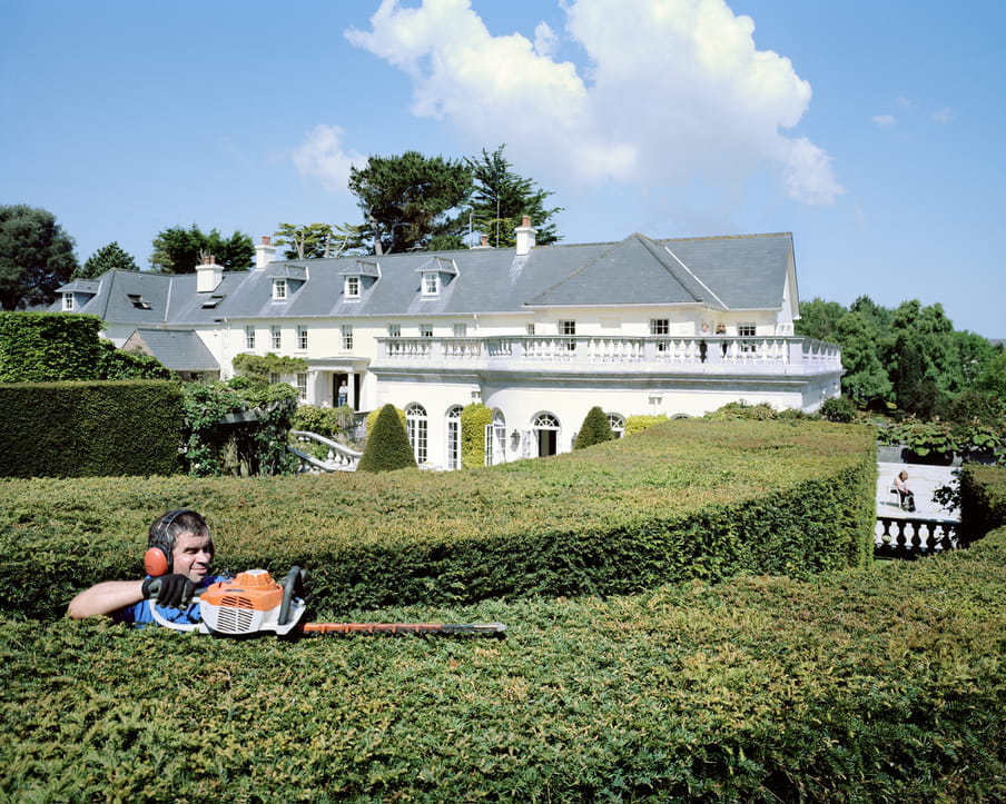 Picture of a large, white mansion and a gardener working in the yard