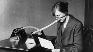 Black and white photograph of a woman reading while wearing a breathing mask on her nose.