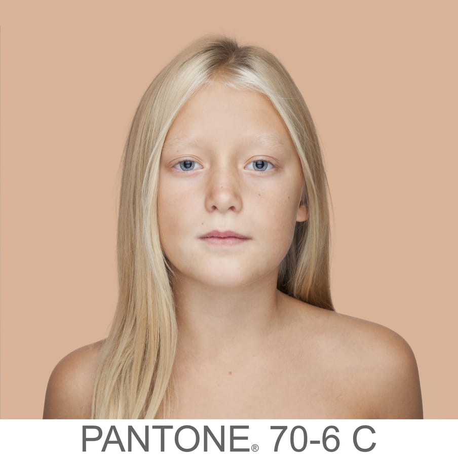 Photographic portrait of a young girl with long blonde hair. The background is a sample of 11 x 11 pixels taken from the nose of the subject and matched with the industrial pallet Pantone®. The pantone color is written out as PANTONE 70-6C.