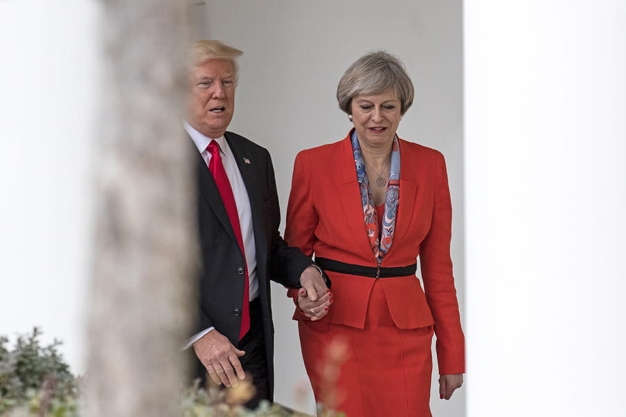 A man wearing a suit is holding the hand of a women in an orange outfit while they are walking.