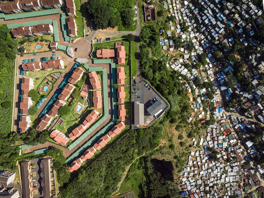 Drone photo of a land. On the left a shanty town, on the right a residential aerea. 