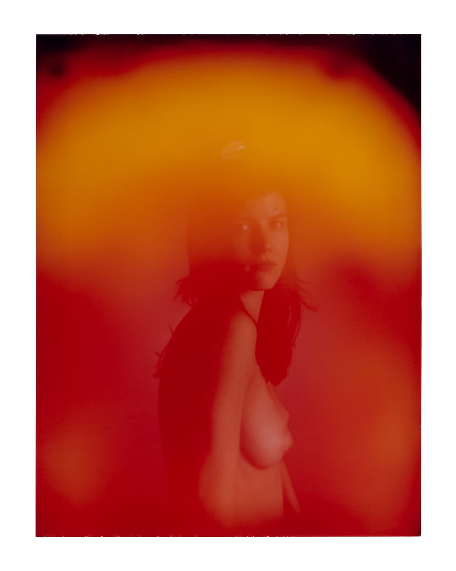 Portrait of a woman with no shirt on and dark hair. A orange, red and black glow covers the image.