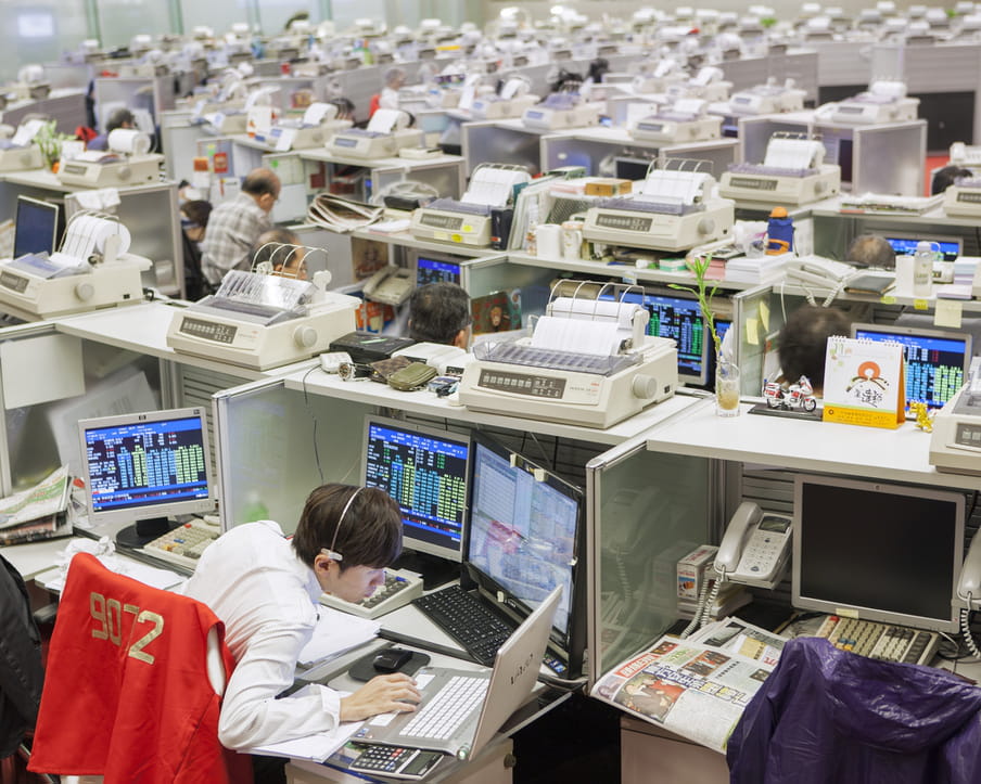 Picture of a crowed stock exchange with people sitting in small cubicles 