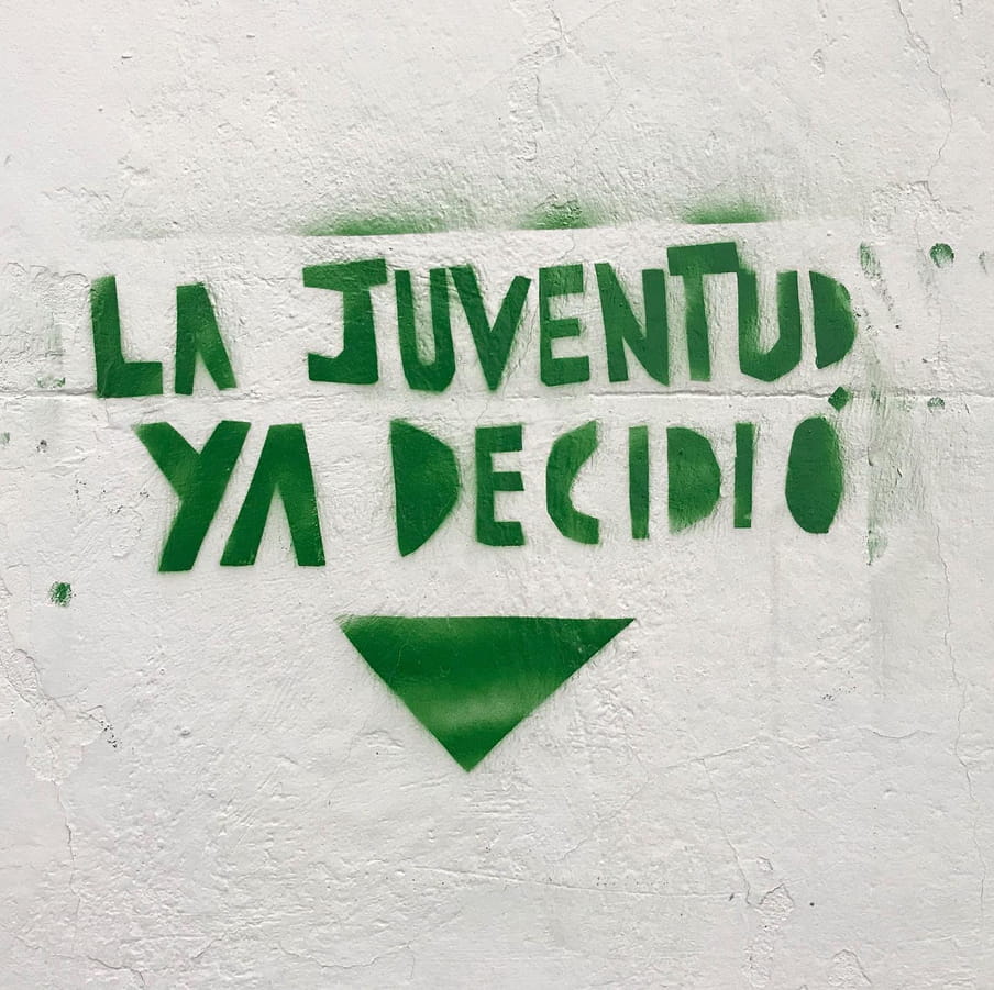 Image of a graffiti in green letters against a white wall. 