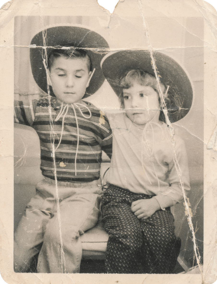 Old damaged sepia coloured photograph of two young children with an arm over the other, seated, and wearing big cowboy hats