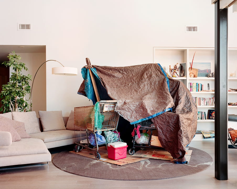 Photo of a living room of a middle or upper class house, with a homeless shelter built from shopping carts and tarp