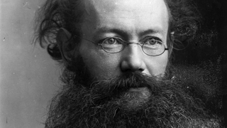 Black and white archival photographic portrait of a bolding man with a beard and glasses. 
