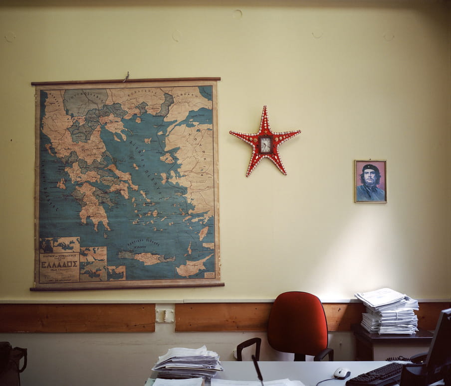 A map of Greece on the wall of an empty office beside a portrait of Che Guevara.  