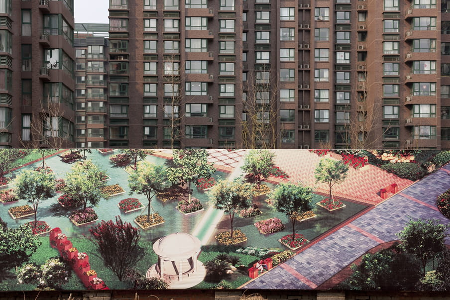 Huge pannel showing a photograph of a surreal aqua garden with pink and purple colours in front of brown buildings. 