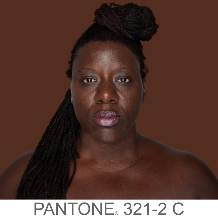 Photographic portrait of a woman with braids in a bun. The background is a sample of 11 x 11 pixels taken from the nose of the subject and matched with the industrial pallet Pantone®. The pantone color is written out as PANTONE 321-2C.