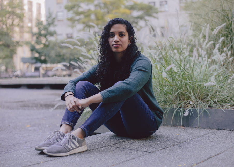 Portrait of a woman with dark curly hair, sitting on the street looking into the camera. 