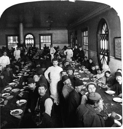 Immigrants seated in the dining hall at Ellis Island, while waiters stand nearby. Photo by Getty